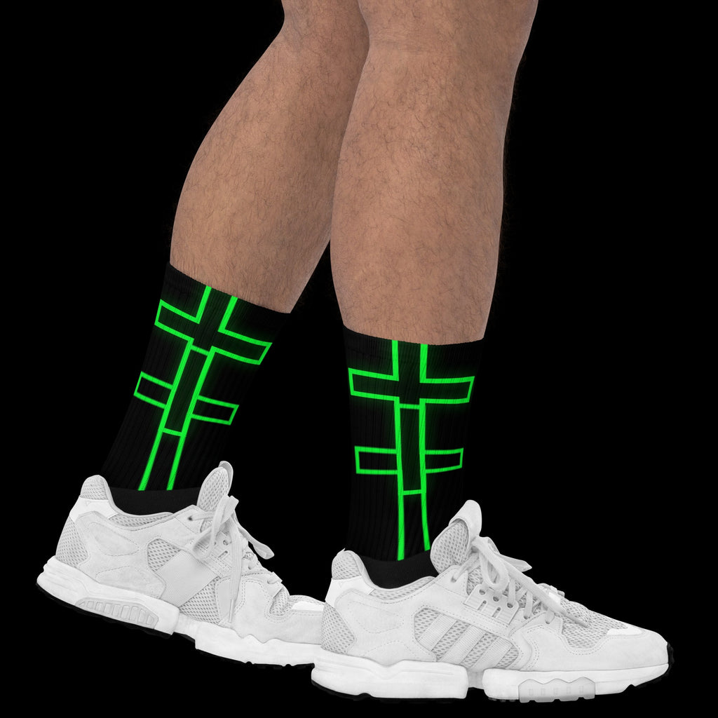 Street Culture crew socks with black base and neon green cross graphic, worn with white sneakers on black background